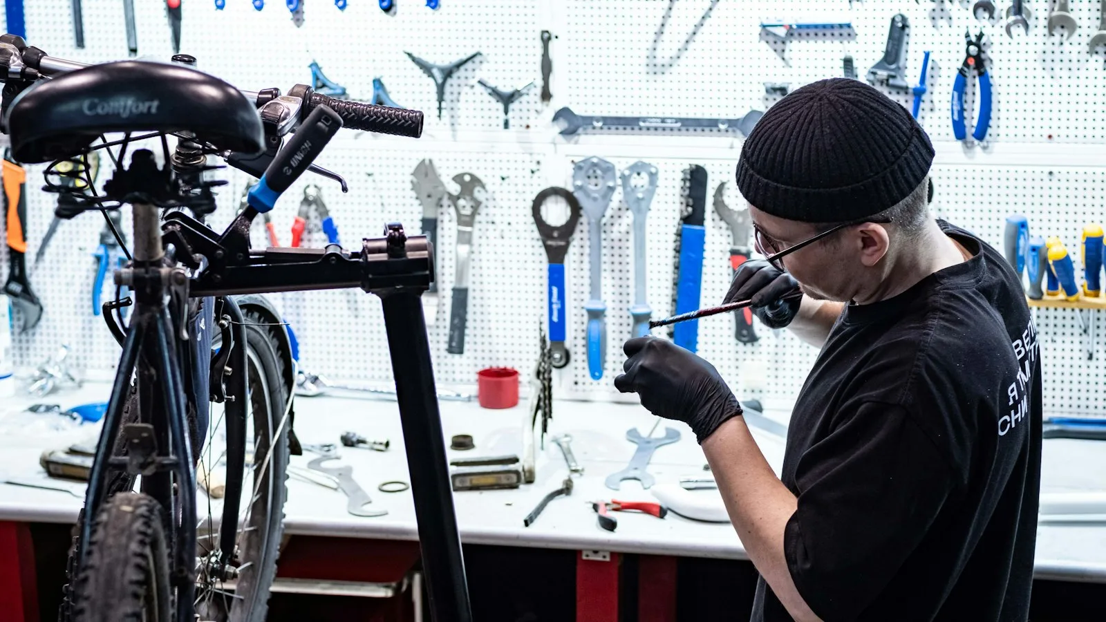 Bicycle mechanic working on a bike in a repair stand in the workshop, with a tool wall behind him