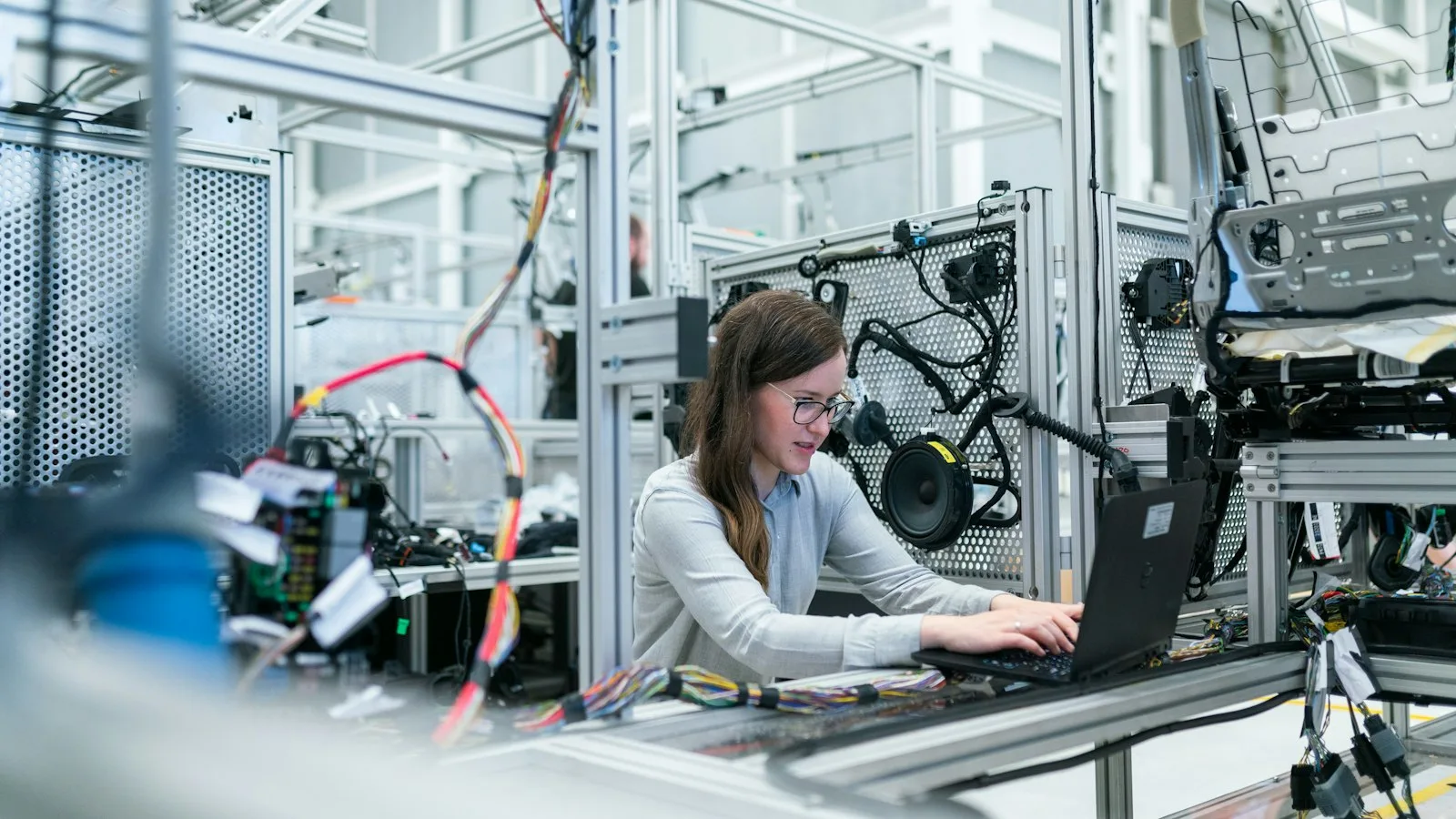 Elektronik-Ingenieurin arbeitet im Testlabor am Laptop, umgeben von Kabelbäumen und Prüfaufbauten